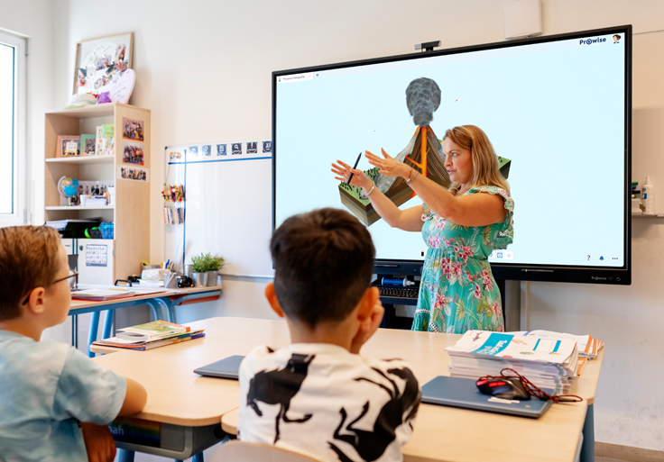 Leerkracht geeft uitleg voor de klas en een Prowise touchscreen, waarop Prowise Presenter wordt gebruikt